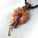 Peach gemstone donut is wire wrapped in copper wire